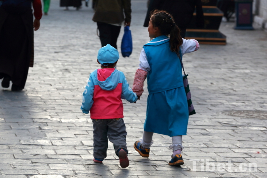 Photo shows two children walking hand in hand on the Barkhor Street. [Photo/ China Tibet Online]