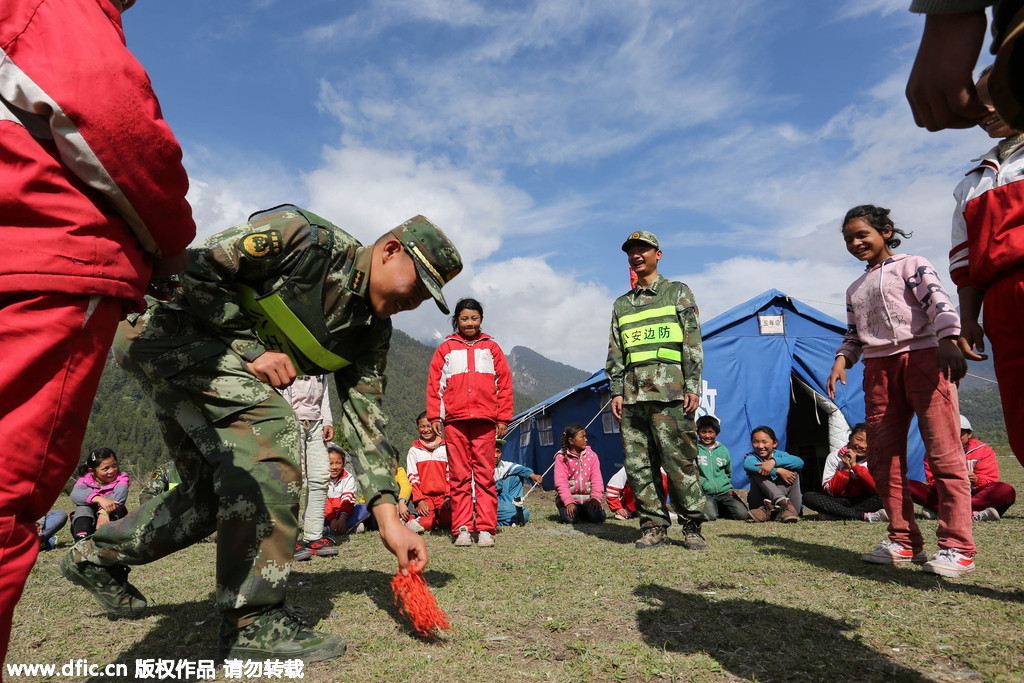 Soldiers of public security frontier forces in Gyirong, Tibet Autonomous Region, who are helping to relocate a makeshift school to more open, safer flatlands, play games with the pupils.[Photo/IC]