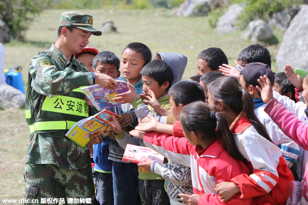 A soldier hands out books to pupils at a makeshift school, at quake affected Gyirong county, Shigatse City of Southwest China's Tibet Autonomous Region on Wednesday. Twenty soldiers of public security frontier forces help relocate the makeshift school to more open, safer flatlands, bringing books, clothes and other necessities.[Photo/IC]