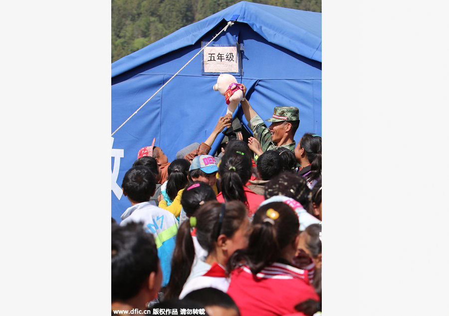 A soldier hands out stuffed toys to pupils at a makeshift school, at quake affected Gyirong county, Shigatse City of Southwest China's Tibet Autonomous Region on Wednesday. Twenty soldiers of public security frontier forces helped relocate the makeshift school to more open, safer flatlands, bringing books, clothes and other necessities.[Photo/IC]