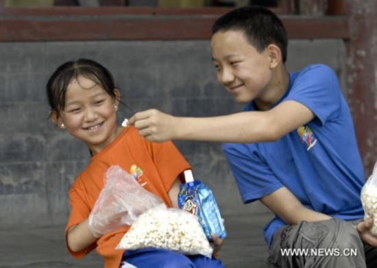 Shang Haiwang (R) and his younger sister Shang Haijiao share popcorn at the Summer Palace in Beijing, capital of China, Aug. 30, 2010.