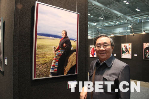  Huang Tingrong takes a photo with one of his favorite pictures at the "Beauty of Tibet" Painting and Photography Exhibition 2013.[Photo/China Tibet Online]