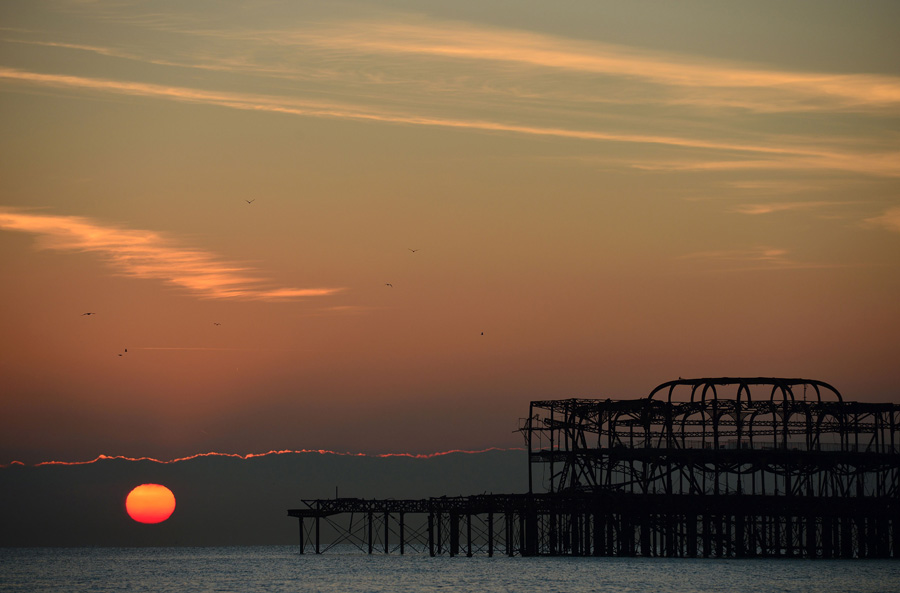 The sun rises over the horizon beyond the West Pier in Brighton on the south coast of England on January 20, 2016. [Photo/CFP]