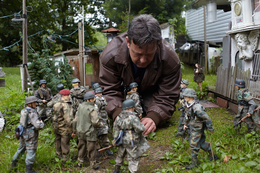 Mark Hogencamp in his garden adjusts some of his 1/6th figures of SS men and paratroopers. Mark Hogancamp nearly died after being jumped by five men in 2000. After waking from a coma with no memories, he developed an extraordinary coping device: he built a miniature town in his garden where he reimagines the horrors of war. [Photo/CFP]